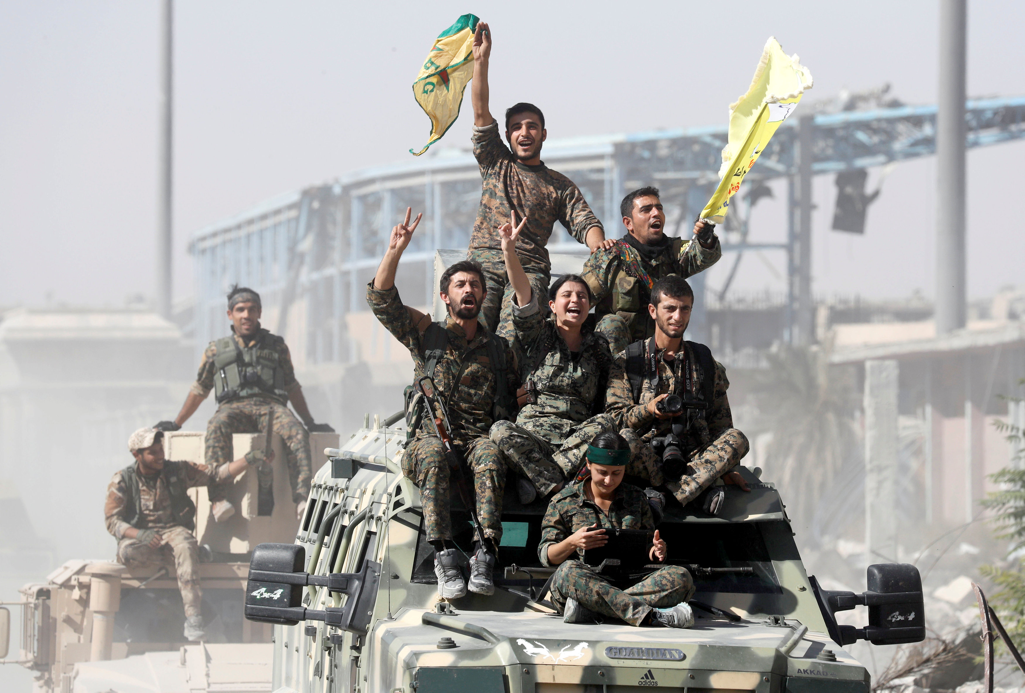 SDF fighters ride atop military vehicles as they celebrate victory in Raqqa